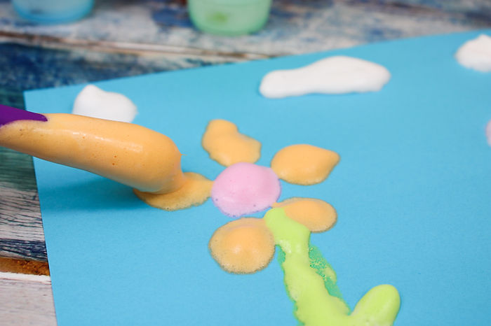 A photo of a picture of flowers and clouds made with puffy paint.