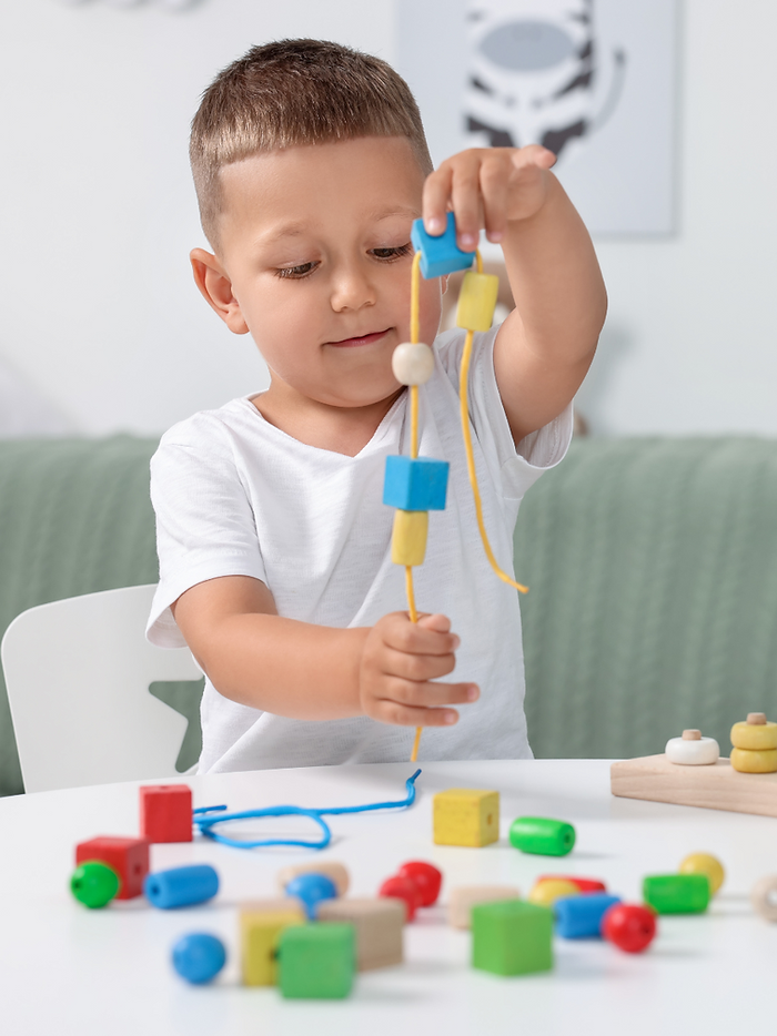 A child putting bead blocks on a string.