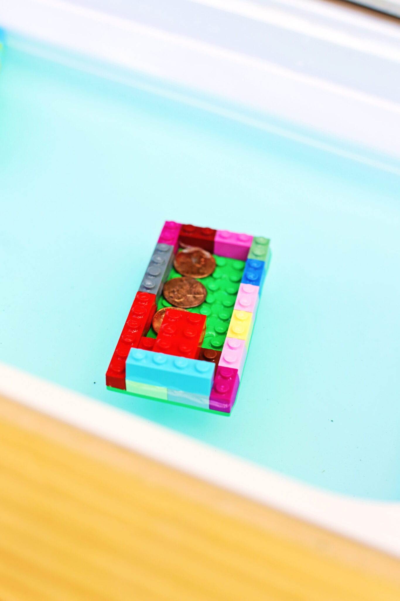 a lego boat in water with two pennies on top