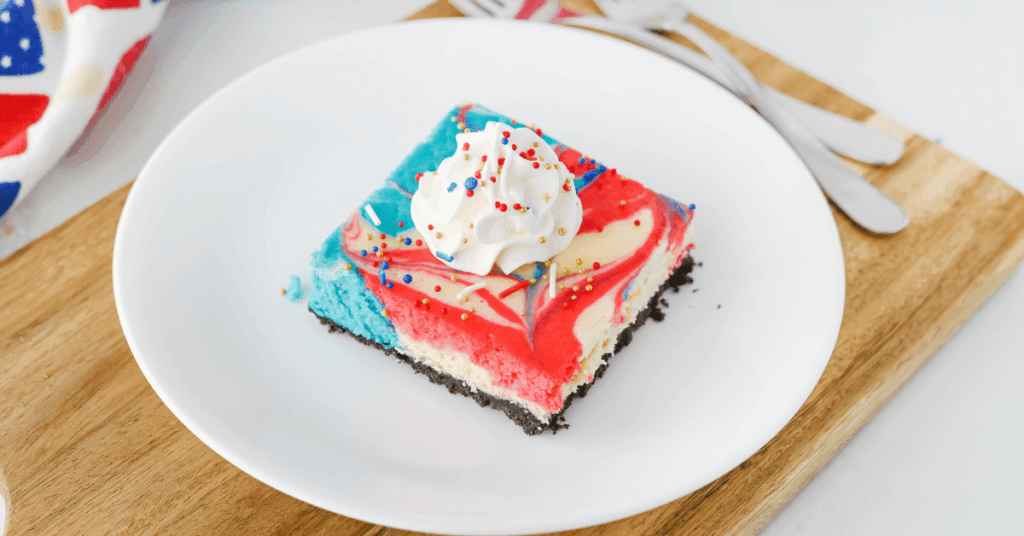 cheesecake bars that have a red and blue swirl, topped with whipped cream and patriotic sprinkles
