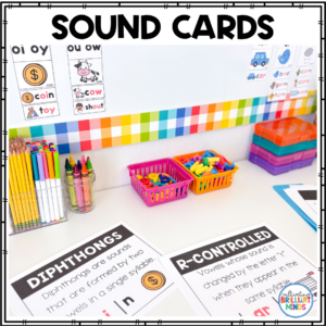 Classroom desk with phonics sound cards (Diphthongs and R-controlled), colorful border, pencil cups, and baskets of letter tiles.