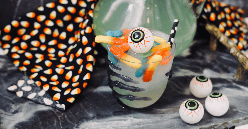 a glass of punch with gummy worms and a plastic eyeball with a black and white polka dot straw