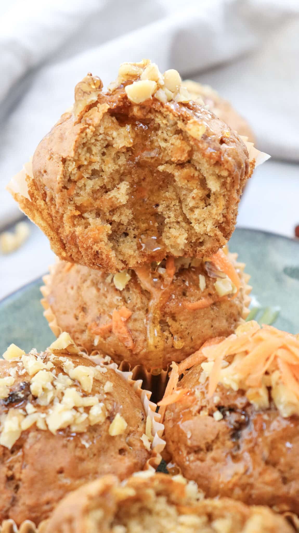 carrot cake muffins stacked on top of each other. the top one has a bite taken out