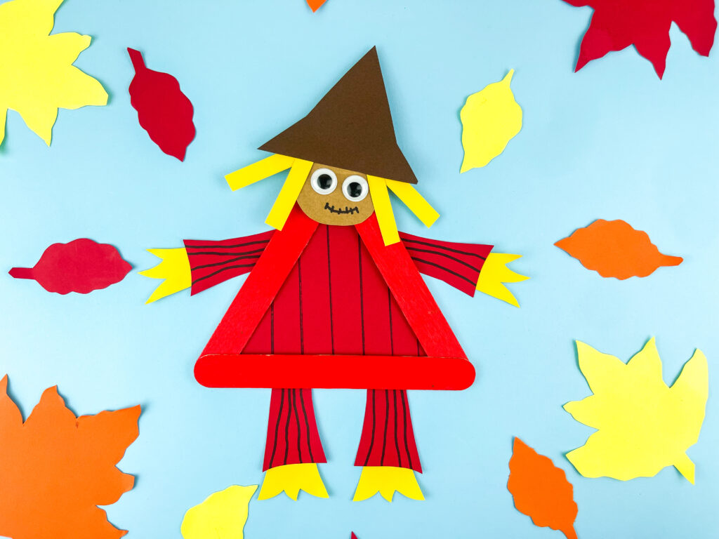 Photo 7-15-25 9 58 39 PM - Cultivating Brilliant Minds scarecrow popsicle craft on blue paper surrounded by construction paper leaves