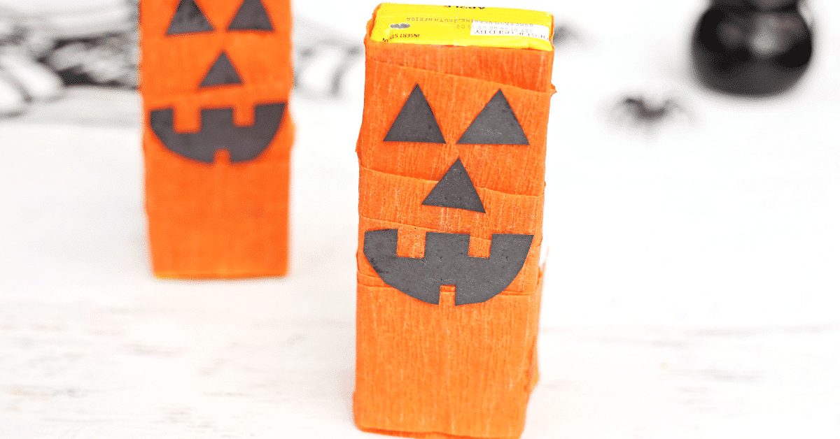 a juice box wrapped in orange streamer with a construction paper jack o lantern face glued on