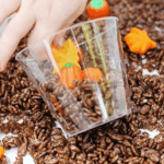 Edible Pumpkin Patch Sensory Bin - Cultivating Brilliant Minds Kid putting the pumpkins and leaves in a cup