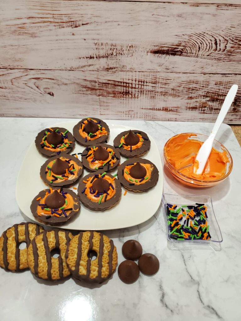 Copy of 20230924_102111 - Cultivating Brilliant Minds chocolate witch hats on a white plate with striped cookies, sprinkles, icing, and hershey kisses