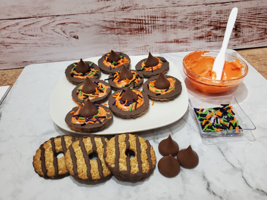 Copy of 20230924_102121 - Cultivating Brilliant Minds chocolate witch hats on a white plate with striped cookies, sprinkles, icing, and hershey kisses