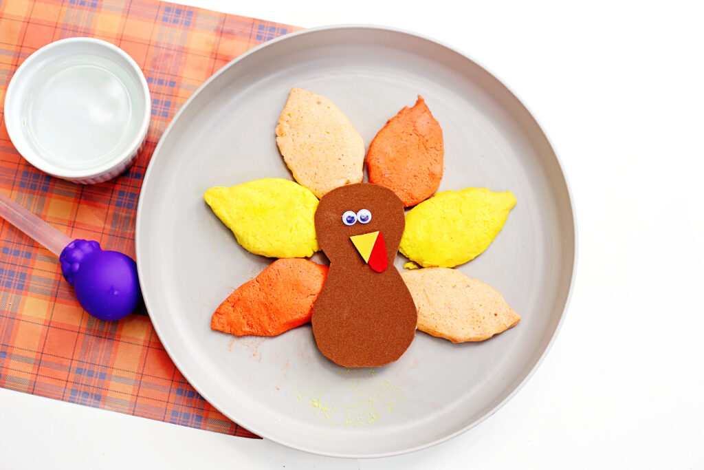 Fizzy Turkey Feather Experiment 1 - Cultivating Brilliant Minds turkey with baking soda feathers on a plate next to a jar of vinegar