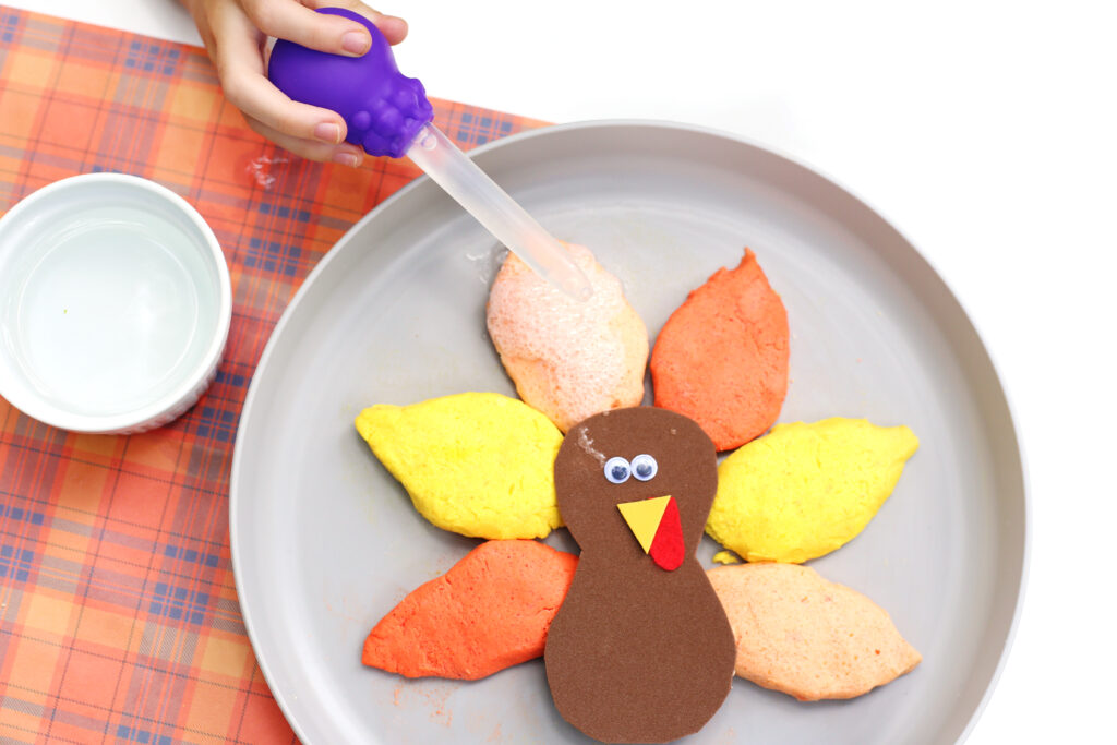 Fizzy Turkey Feather Experiment 2 - Cultivating Brilliant Minds a kid squeezing vinegar onto the baking soda feathers