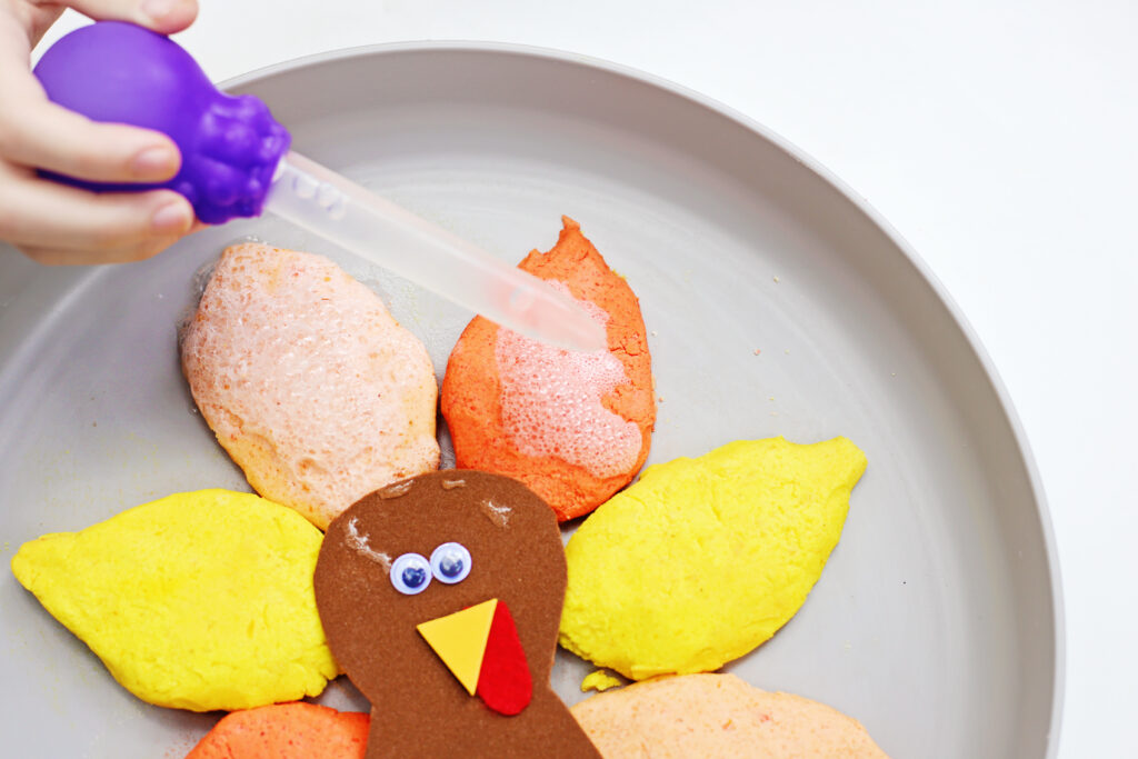 Fizzy Turkey Feather Experiment 3 - Cultivating Brilliant Minds a kid squeezing vinegar onto the baking soda feathers