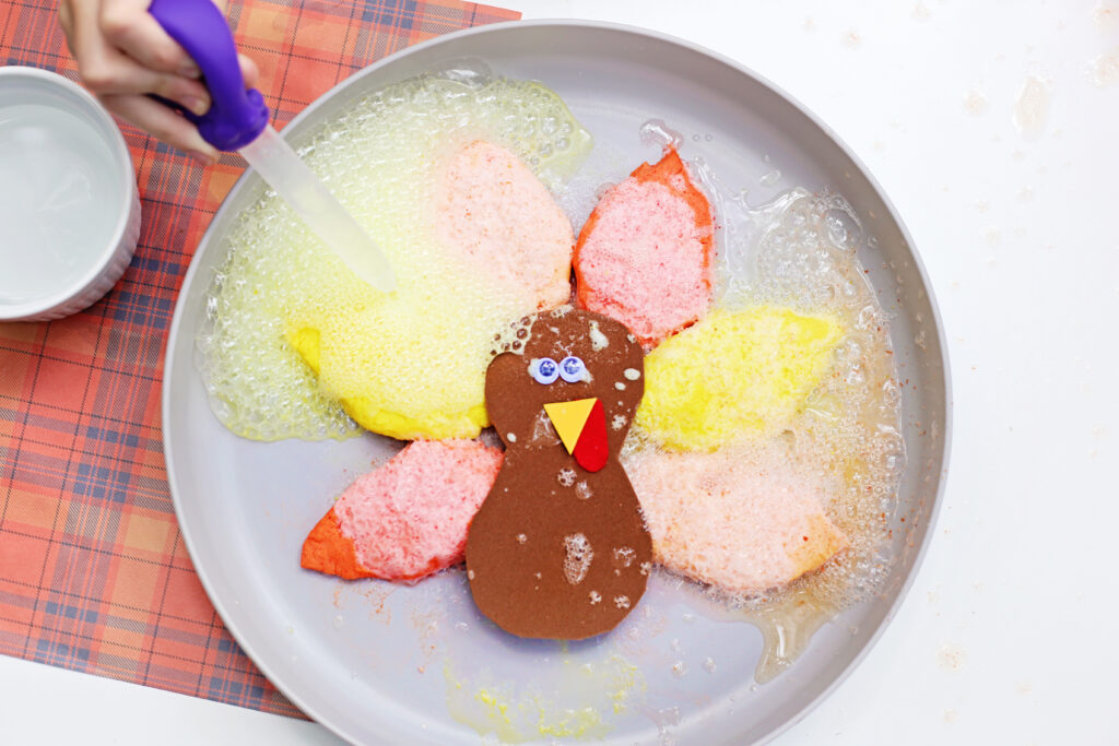 Fizzy Turkey Feather Experiment 5 - Cultivating Brilliant Minds a kid squeezing vinegar onto the baking soda feathers