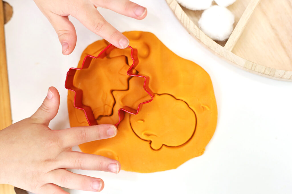 Pumpkin Pie Playdough Tray 3 - Cultivating Brilliant Minds a kid using a cookie cutter to cut out shapes in the playdough