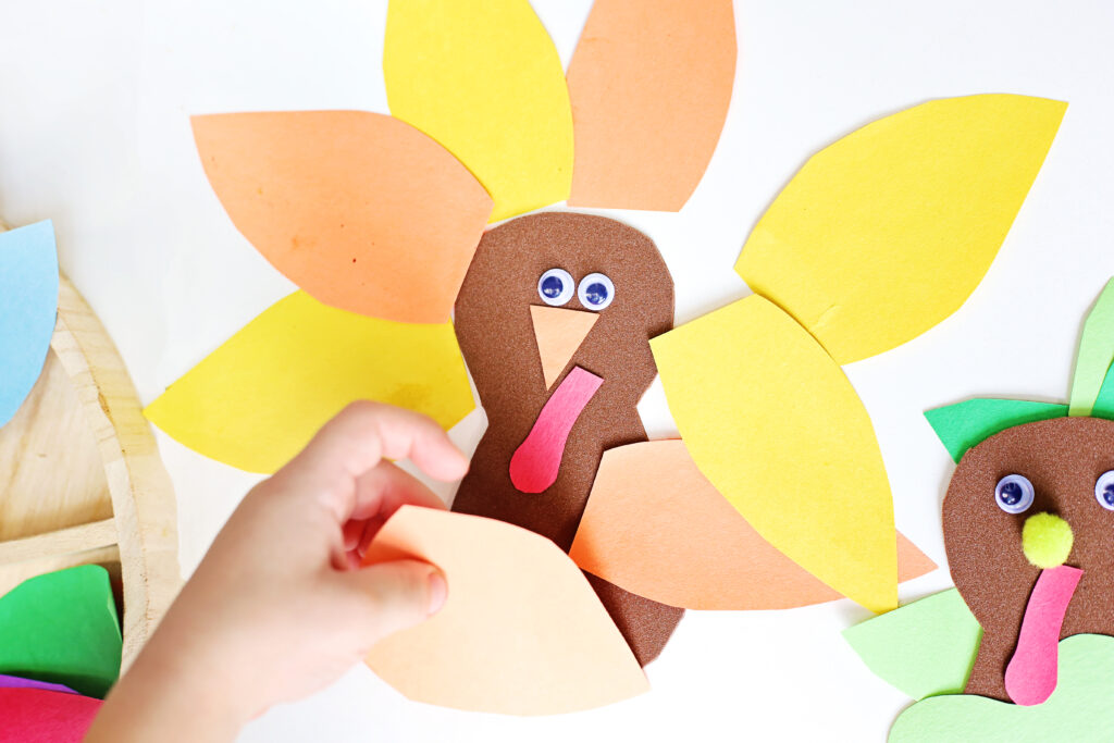 Turkey in Disguise Craft 9 - Cultivating Brilliant Minds a kid's hand decorating a turkey with an orange feather