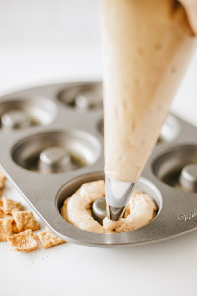 cinnamon toast crunch donuts-29 - Cultivating Brilliant Minds piping the mixture into a donut pan