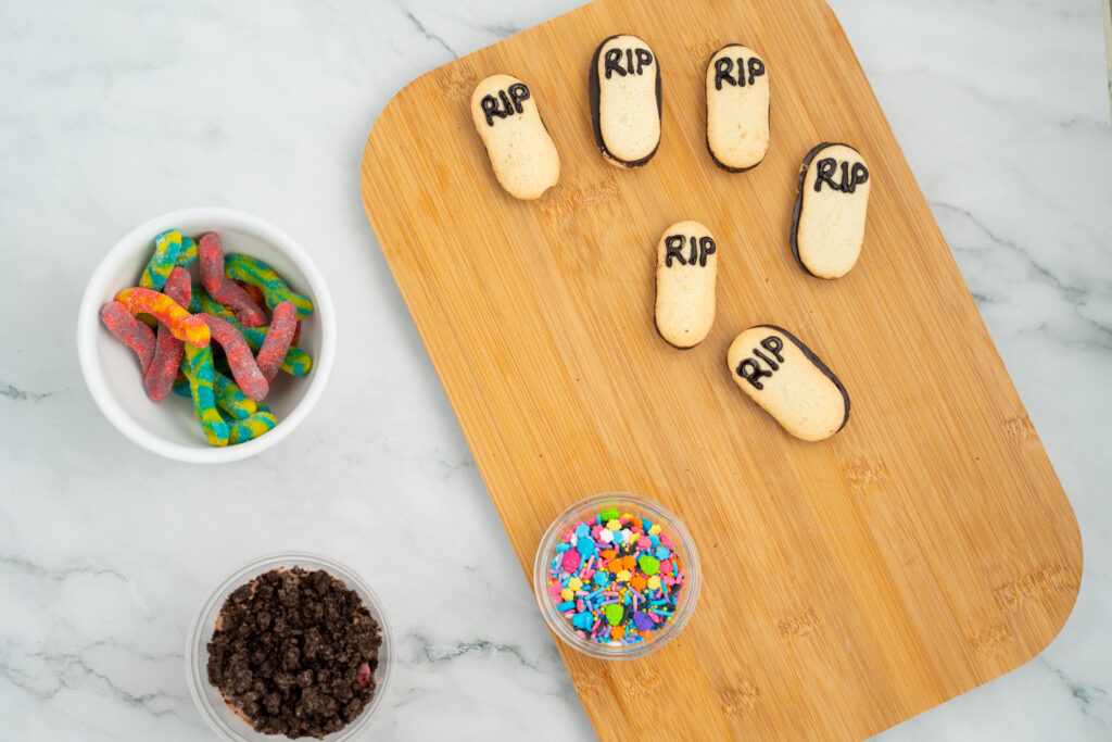 dirtcakecups-07878 - Cultivating Brilliant Minds cookies on a cutting board with sprinkles, gummie worms, and crushed cookies in bowls