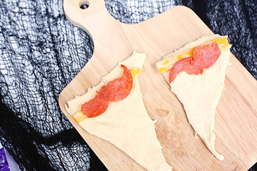 Witch Hat Pizza Snacks For Halloween - Cultivating Brilliant Minds dough cut into a triangle with cheese and pepperoni on it