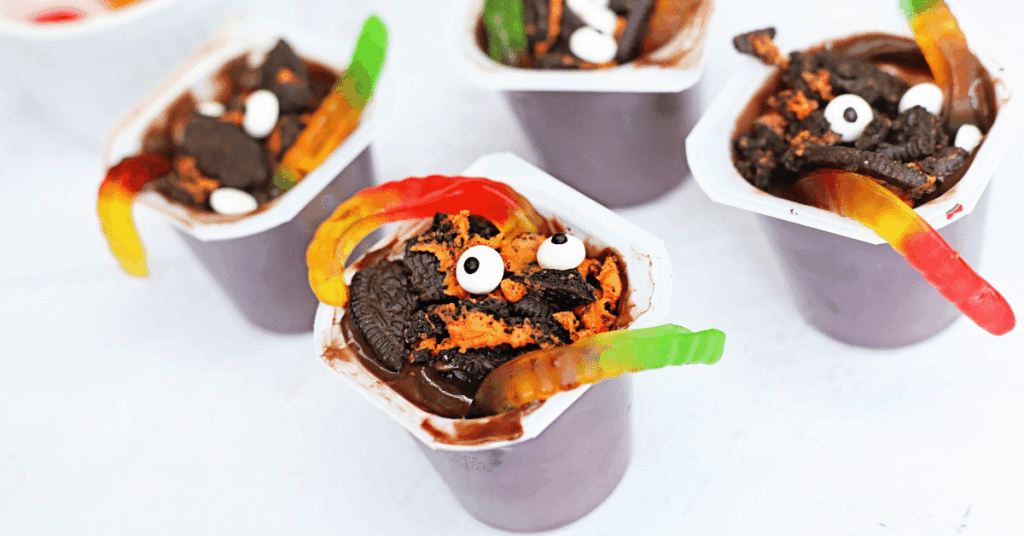 a pudding cup with crushed oreos, gummy worms, and candy eyes