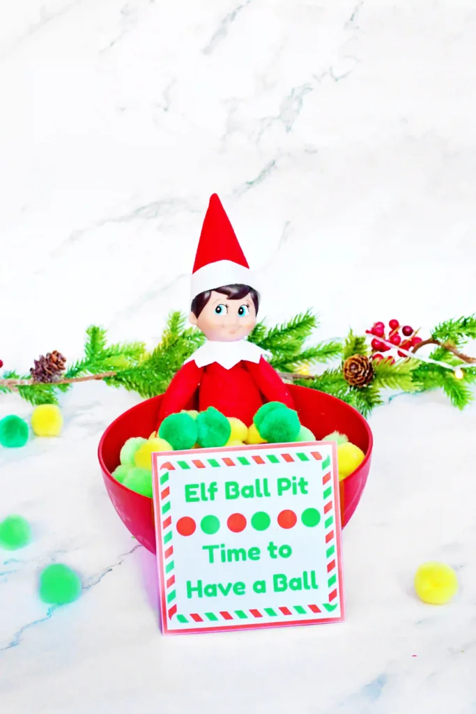 Elf on the Shelf Idea - Cultivating Brilliant Minds elf on the shelf in a bowl of pom poms with a sign that reads "elf ball pit - time to have a ball"