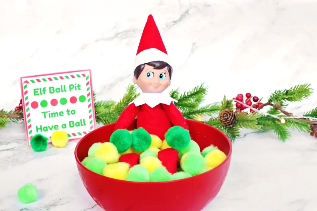 Elf on the Shelf Idea - Cultivating Brilliant Minds elf on the shelf in a bowl of pom poms with a sign that reads "elf ball pit - time to have a ball"