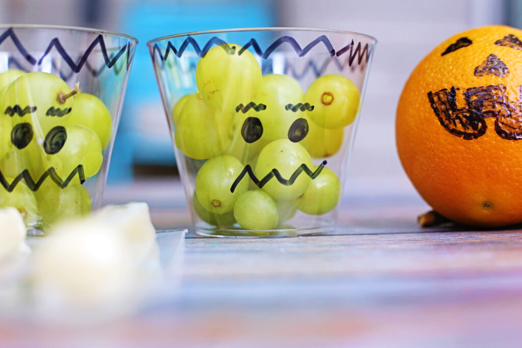 Healthy Halloween Snacks - Cultivating Brilliant Minds frankenstein face drawn on a plastic cup with grapes in it