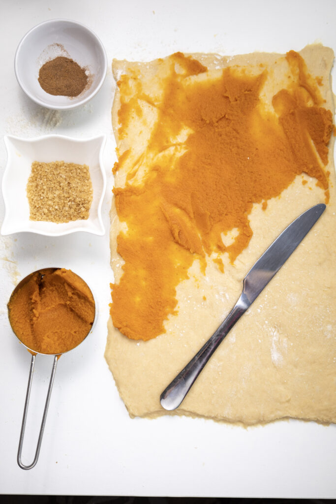 Pumpkin Cinnamon Rolls - Cultivating Brilliant Minds adding cinnamon and sugar to pumpkin cinnamon roll dough