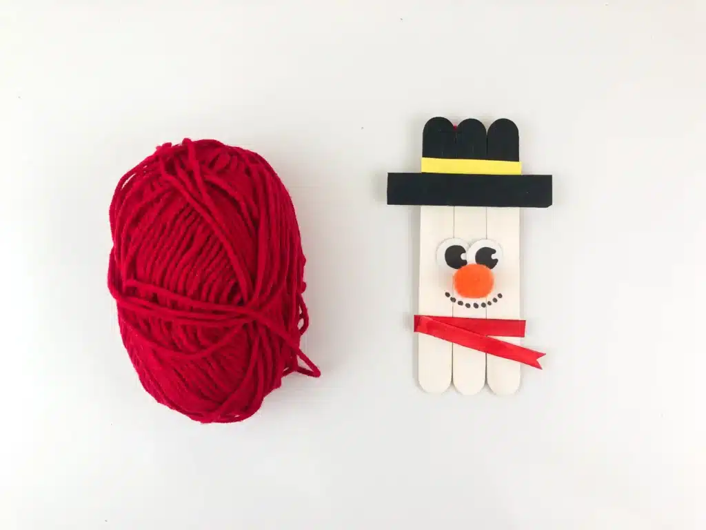 Snowman Popsicle Stick Ornament - Cultivating Brilliant Minds yarn next to a snowman popsicle stick craft