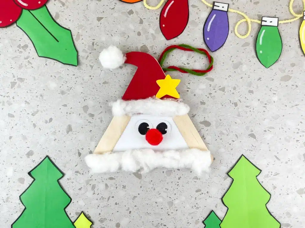 Santa Popsicle Stick Craft - Cultivating Brilliant Minds popsicle sticks glued into a triangle with a red hat, red nose, and cotton ball beard to look like santa
