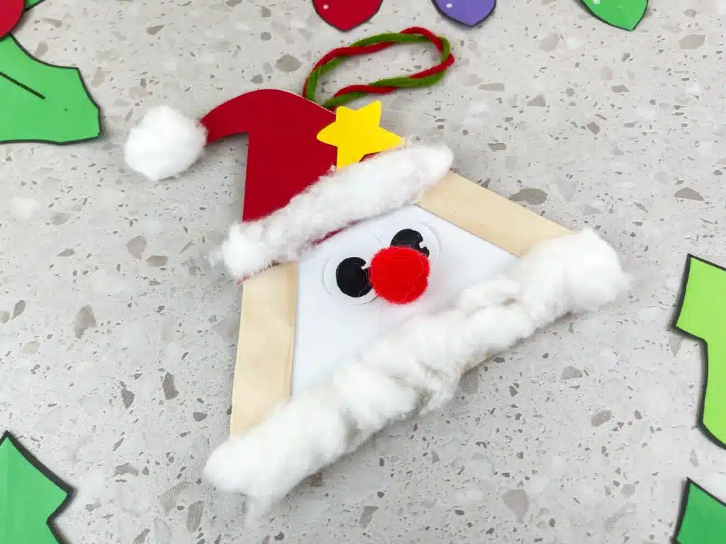 Santa Popsicle Stick Craft - Cultivating Brilliant Minds popsicle sticks glued into a triangle with a red hat, red nose, and cotton ball beard to look like santa