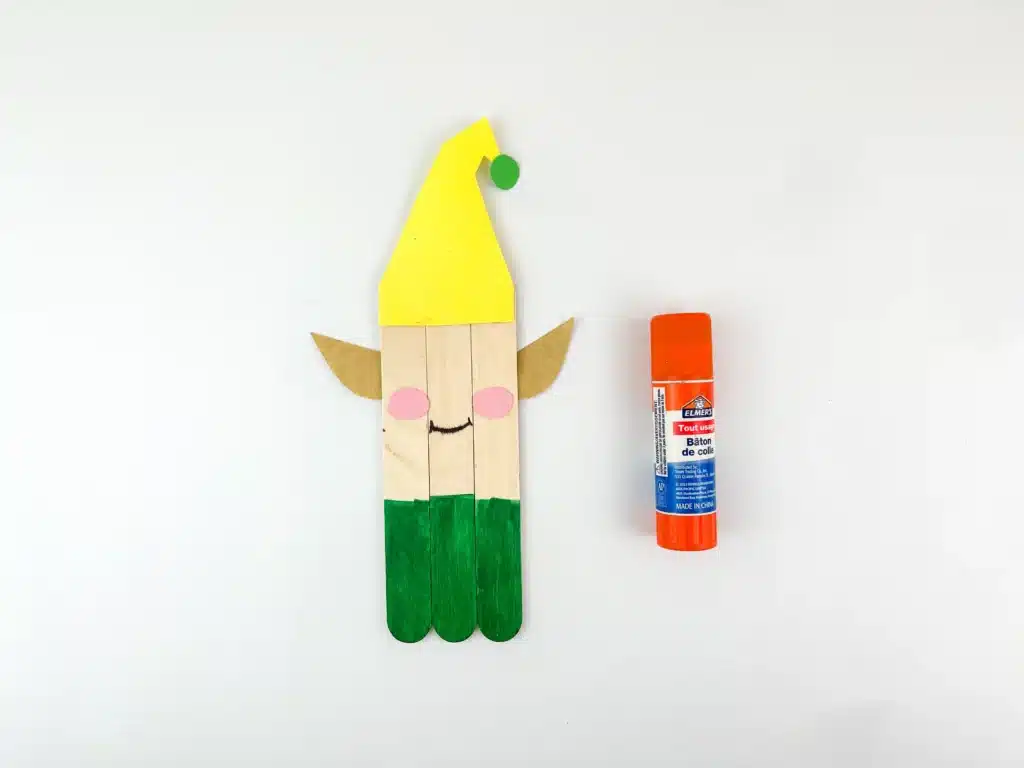 three popsicle sticks glued together with the bottom painted green, a mouth and rosy cheeks, with elf ears and an elf hat