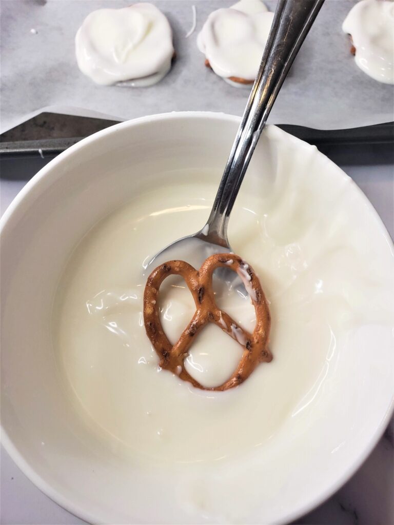 Ghost Pretzels For Halloween - Cultivating Brilliant Minds dipping a pretzel in melted white chocolate