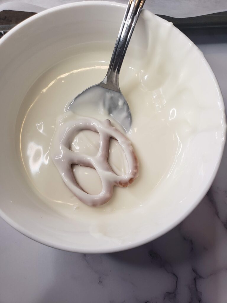 Ghost Pretzels For Halloween - Cultivating Brilliant Minds dipping a pretzel in melted white chocolate