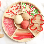 Holiday Cookie Playdough Bakery Tray - Cultivating Brilliant Minds a playdough tray filled with holiday-related items like red and green sprinkles and gingerbread cookie cutters