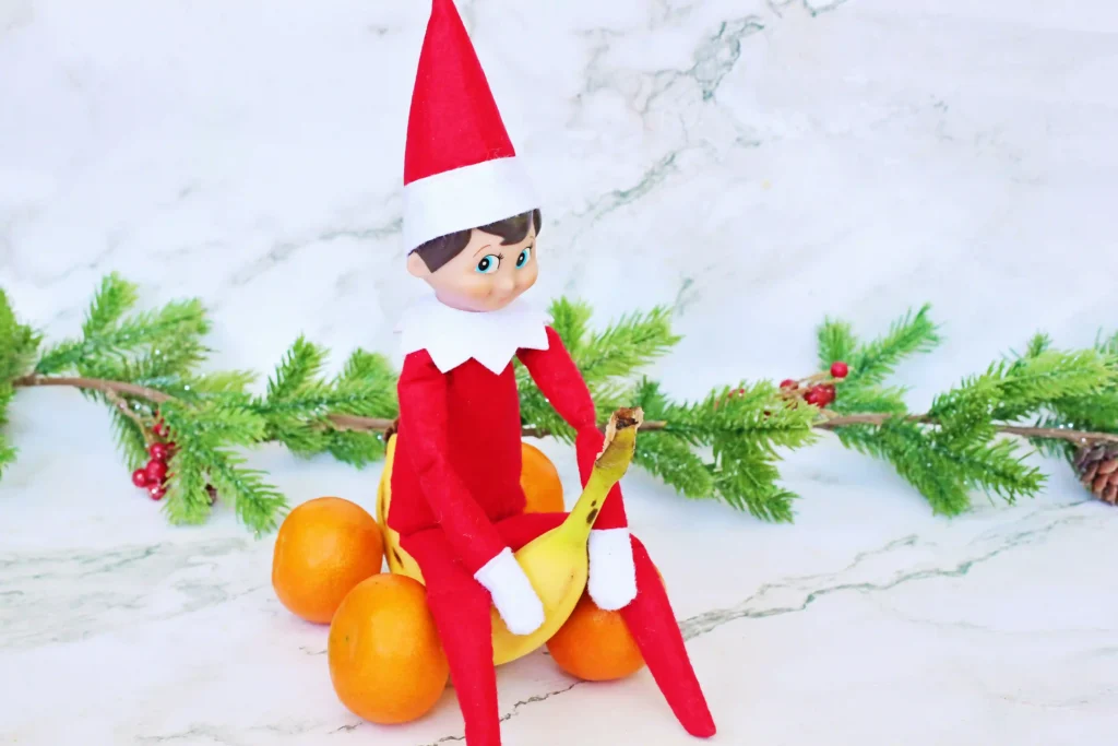 Elf on the Shelf Idea: Banana Races - Cultivating Brilliant Minds an elf on the shelf on a banana made to look like a car with oranges for wheels
