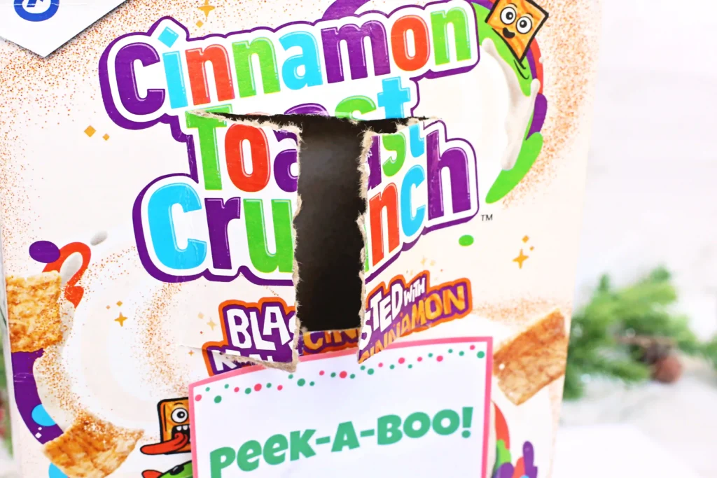 Elf on the Shelf Cereal Box Peekaboo - Cultivating Brilliant Minds a hole cut in a box of cinnamon toast crunch