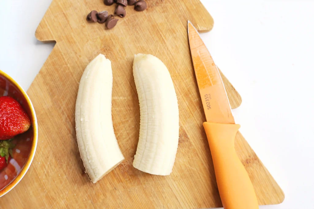 Banana Santa: A Healthy Christmas Snack - Cultivating Brilliant Minds bananas next to a knife on a wooden board that is shaped like a christmas tree
