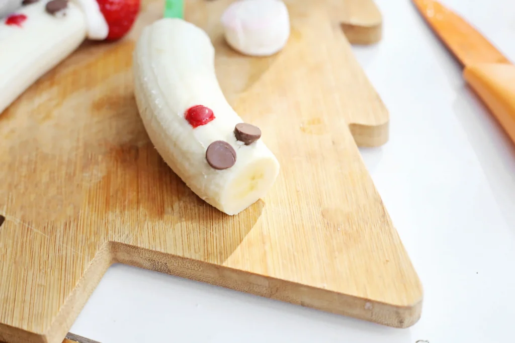 Banana Santa: A Healthy Christmas Snack - Cultivating Brilliant Minds a banana with chocolate chip eyes and an m&m for a mouth