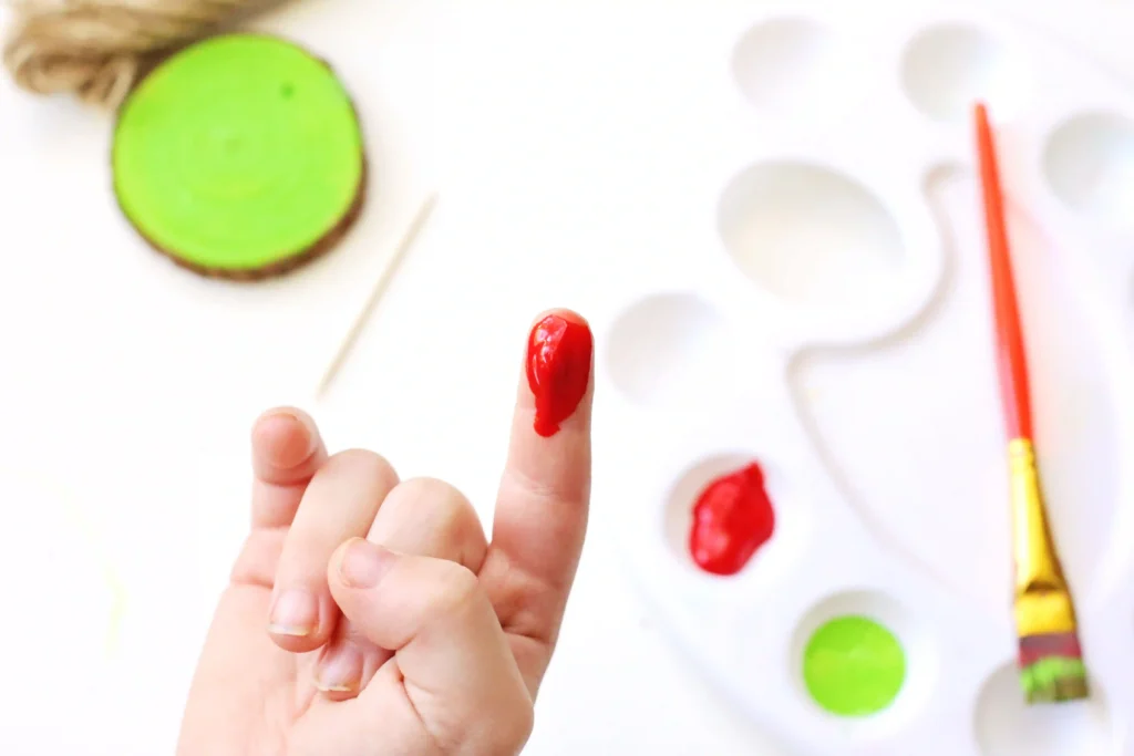Grinch Heart Wood Slice Ornament Craft - Cultivating Brilliant Minds a kid's finger dipped in red paint
