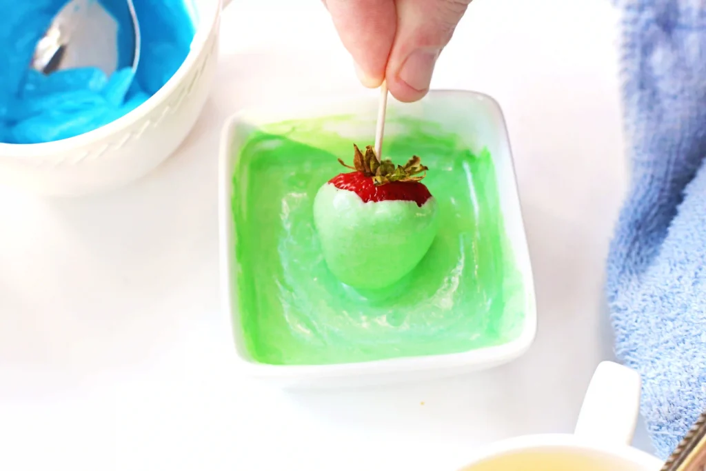 Christmas Light Strawberries - Cultivating Brilliant Minds dipping a strawberry in the colored candy melt