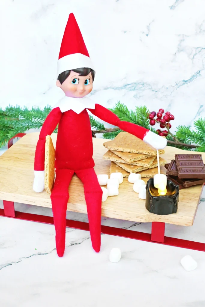 Elf on the Shelf Idea: Elf Campfire - Cultivating Brilliant Minds an elf on the shelf roasting a marshmallow over a flameless candle next to ingredients for s'mores