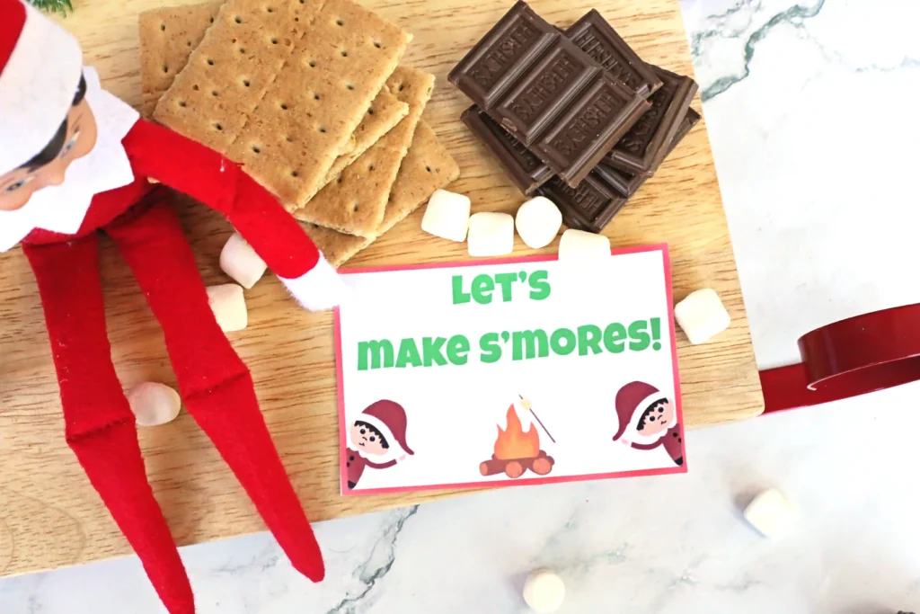 Elf on the Shelf Idea: Elf Campfire - Cultivating Brilliant Minds an elf on the shelf next to ingredients for s'mores with a sign that reads "let's make s'mores!"