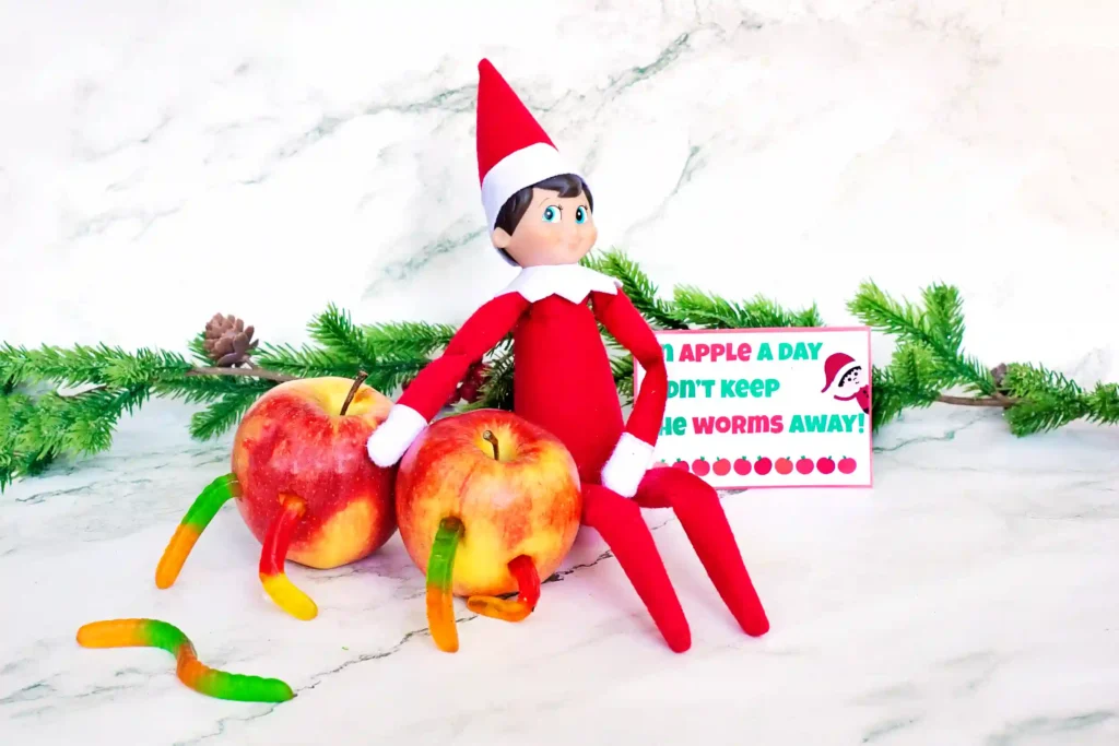 Elf on the Shelf Idea Worms in Apple - Cultivating Brilliant Minds an elf on the shelf next tow apples with gummy worms on them and a sign that reads "an apple a day didn't keep the worms away"