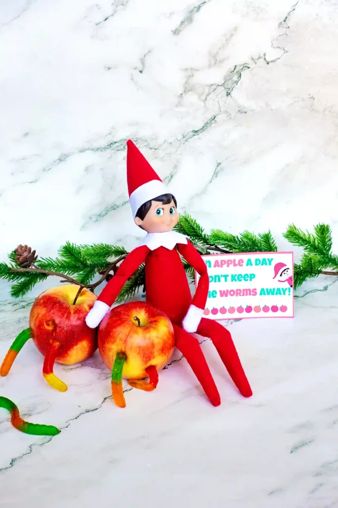 Elf on the Shelf Idea Worms in Apple - Cultivating Brilliant Minds an elf on the shelf next tow apples with gummy worms on them and a sign that reads "an apple a day didn't keep the worms away"