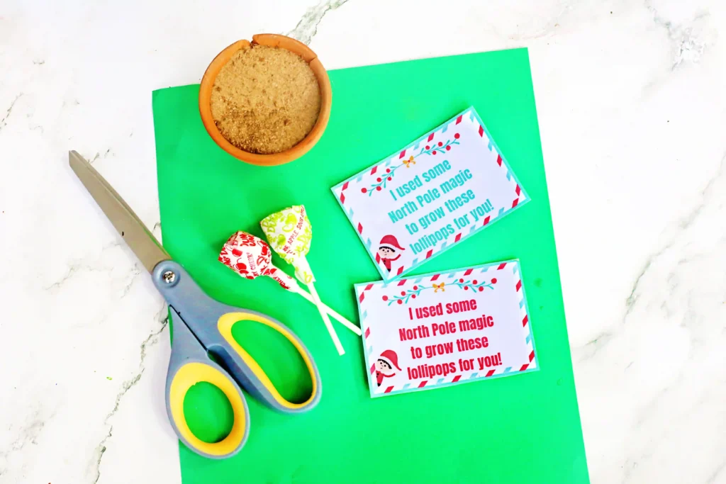 Elf on the Shelf Idea Lollipop Garden - Cultivating Brilliant Minds green construction paper, scissors, lollipops, a flower pot, and a free elf on the shelf printable sign