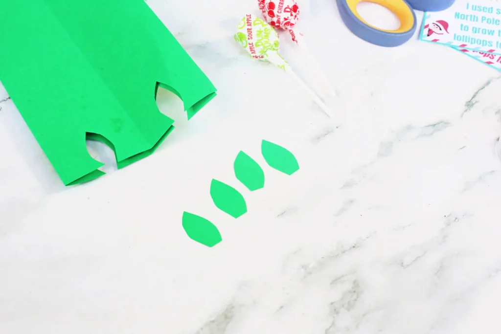 Elf on the Shelf Idea Lollipop Garden - Cultivating Brilliant Minds cutting leaf shapes out of green construction paper