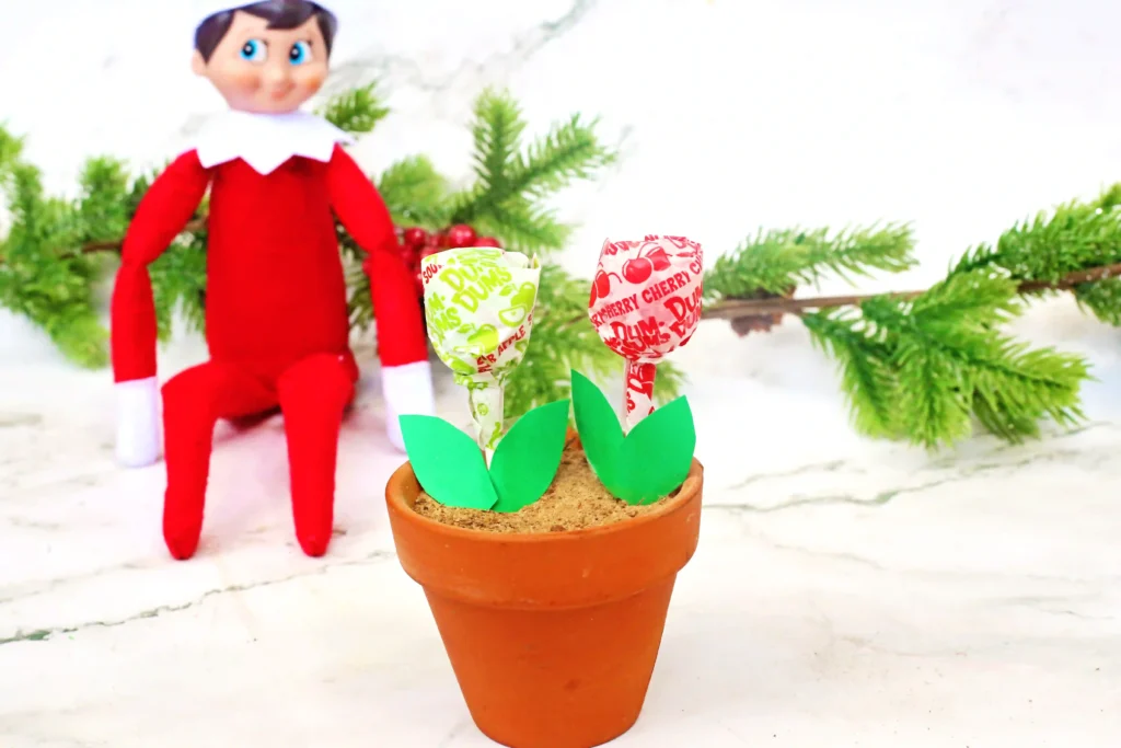 Elf on the Shelf Idea Lollipop Garden - Cultivating Brilliant Minds an elf on the shelf next to a flowerpot filled with lollipops