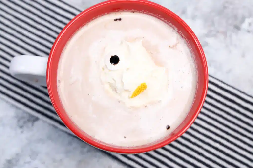 Frozen Whipped Cream Snowman - Cultivating Brilliant Minds frozen whipped cream with candy eyes and a carrot nose to look like a snowman melted in a cup of hot cocoa