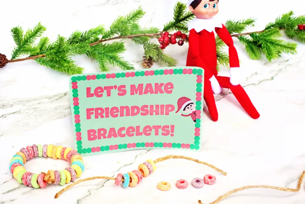 Elf on the Shelf Idea Fruit Loop Bracelets - Cultivating Brilliant Minds an elf on the shelf holding a fruit loop bracelet next to a bowl of fruit loops and a sign that reads "let's make friendship bracelets"