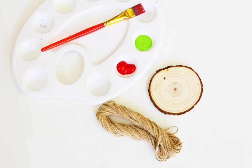 Grinch Heart Wood Slice Ornament Craft - Cultivating Brilliant Minds green and red paint, a paint brush, string, and a wood slice