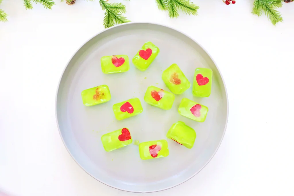 Grinch's Frozen Heart Activity - Cultivating Brilliant Minds ice cubes dyed green with a heart frozen inside on a gray plate